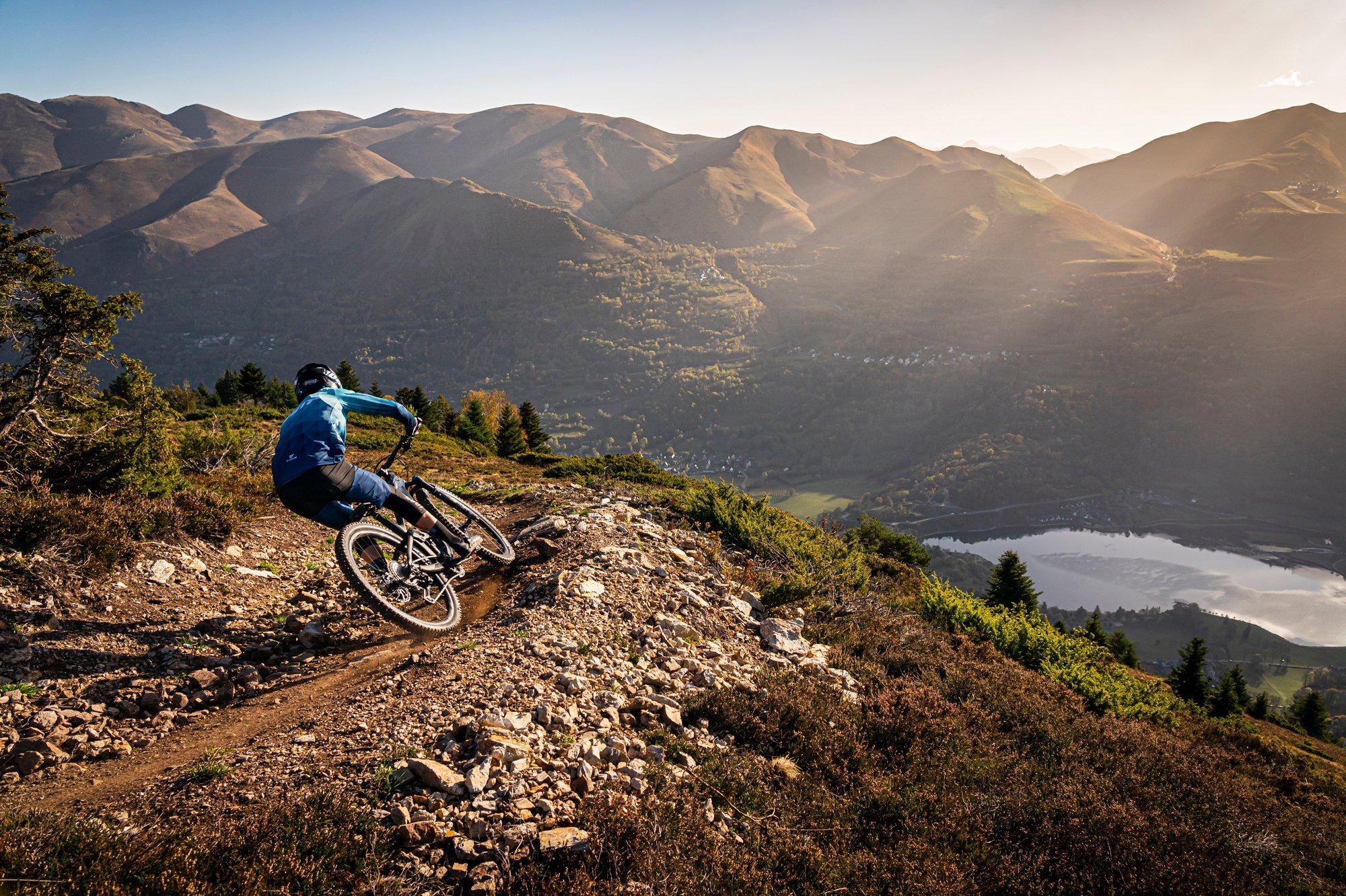 a mountain biker riding down a rocky hillside with a lake in the background