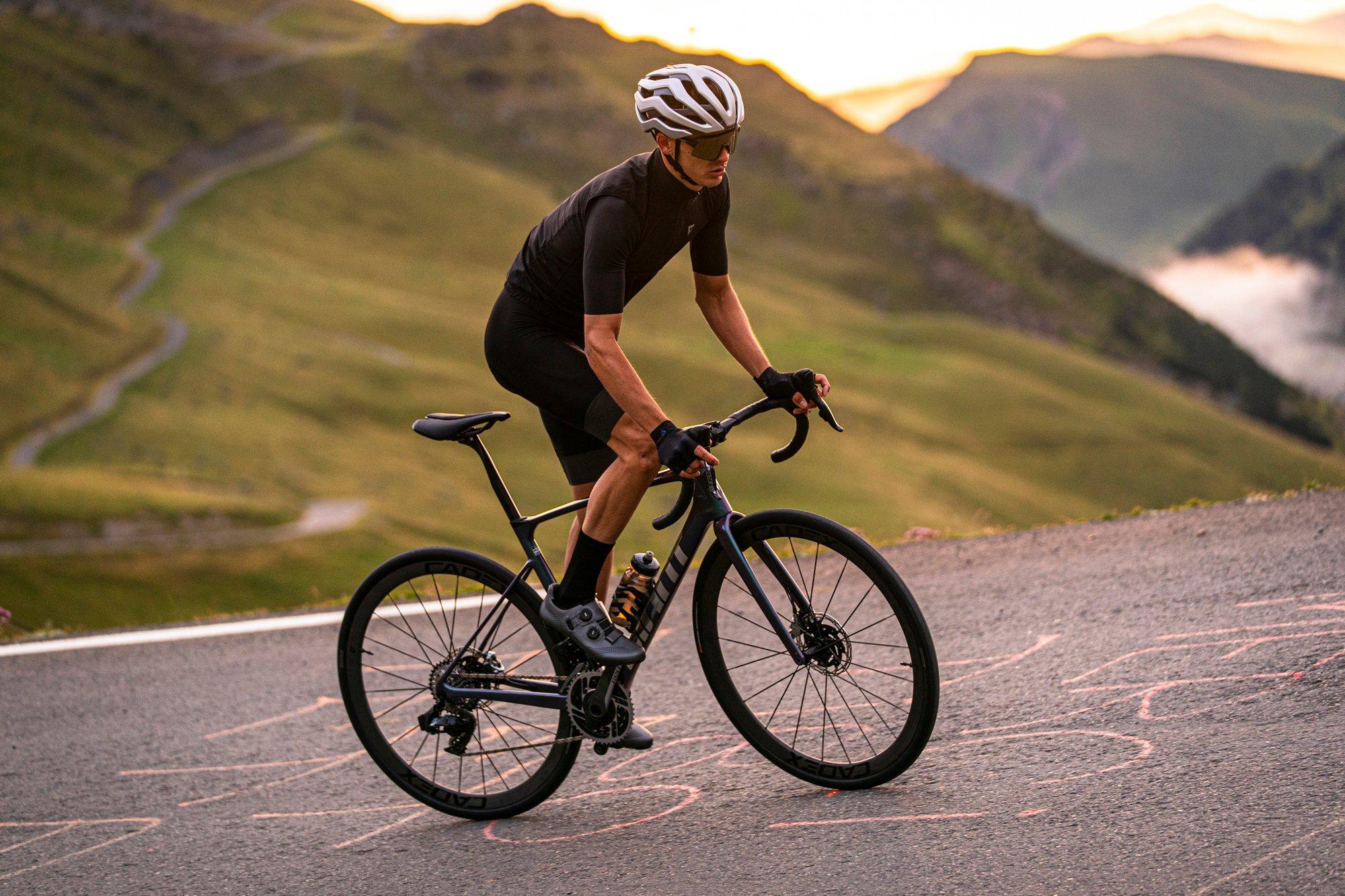 a man riding a bike on a road with mountains in the background