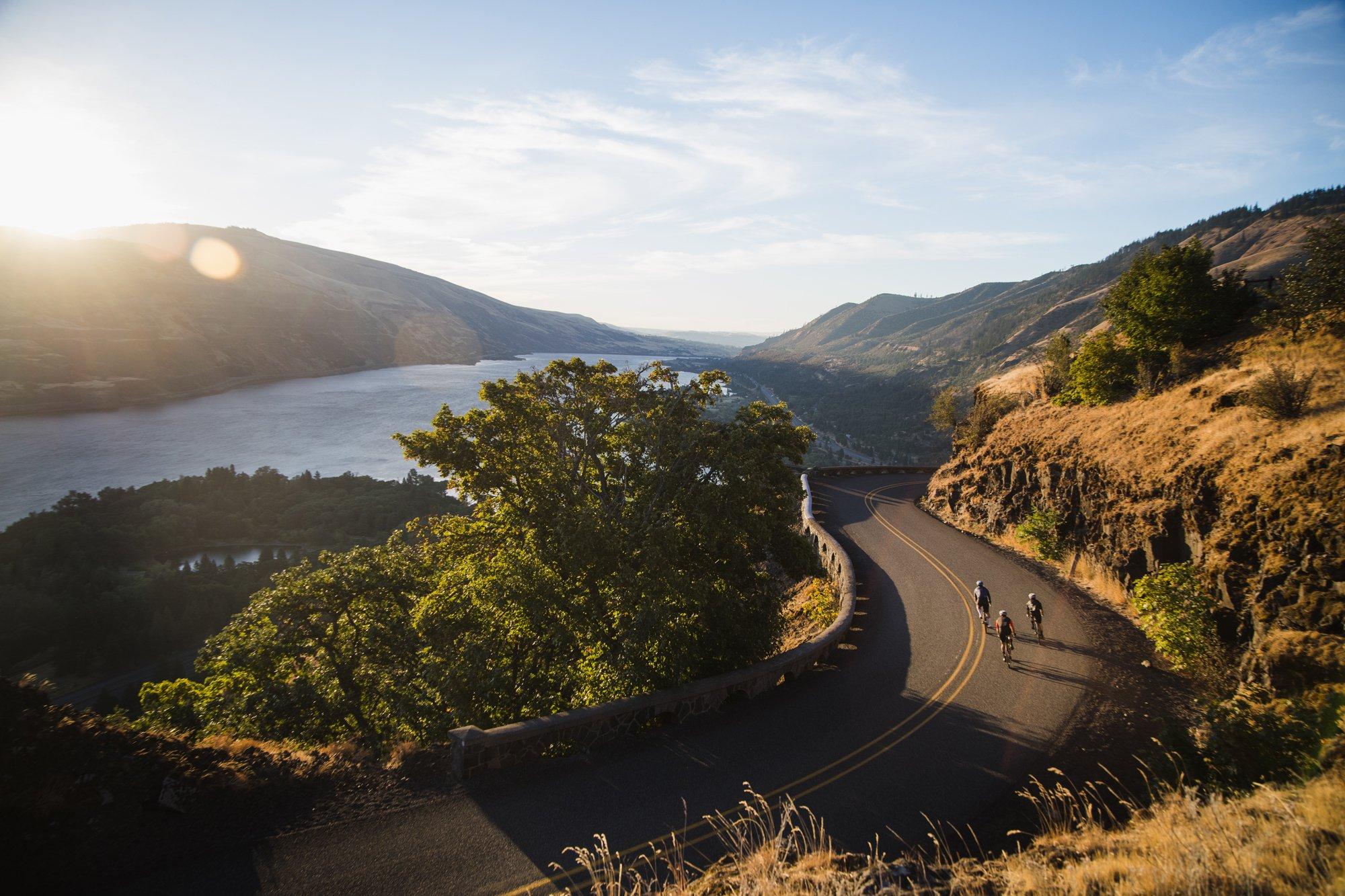 two people riding bicycles down a winding road near a lake
