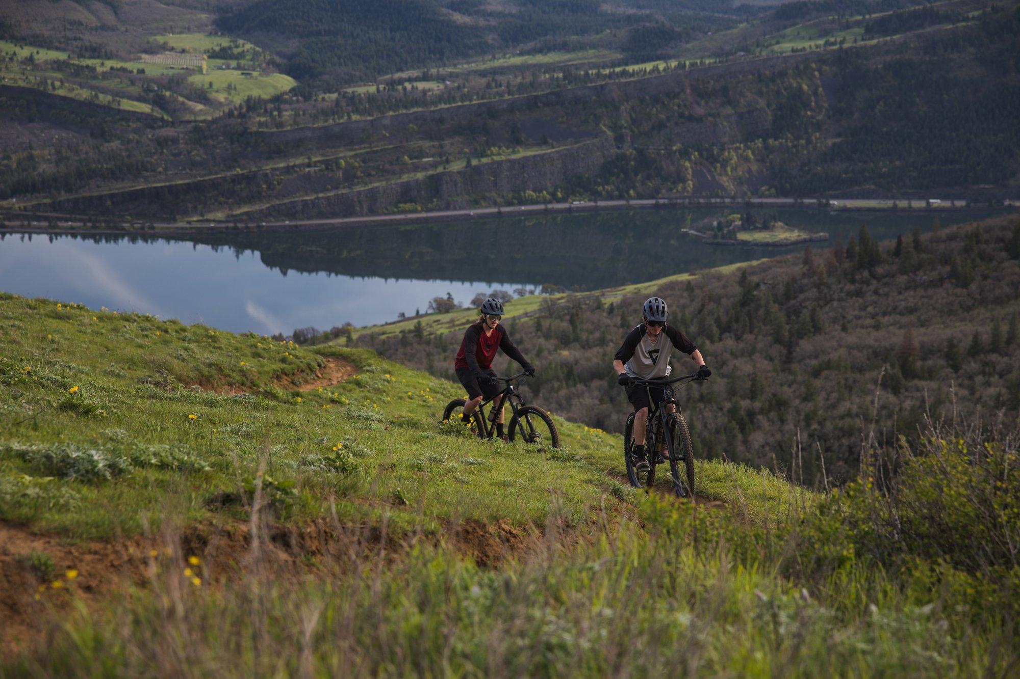 two mountain bikers are riding down a hill near a lake