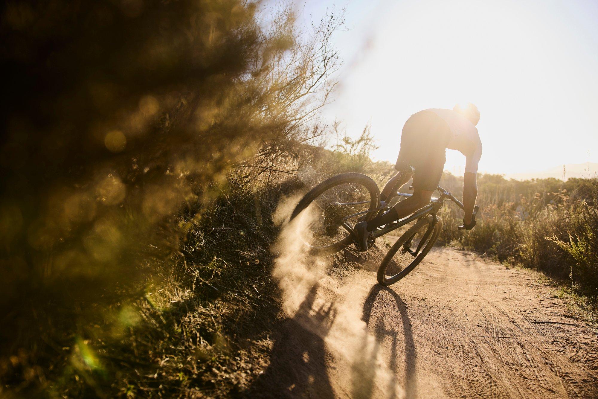 a person riding a bike on a dirt road in the sun