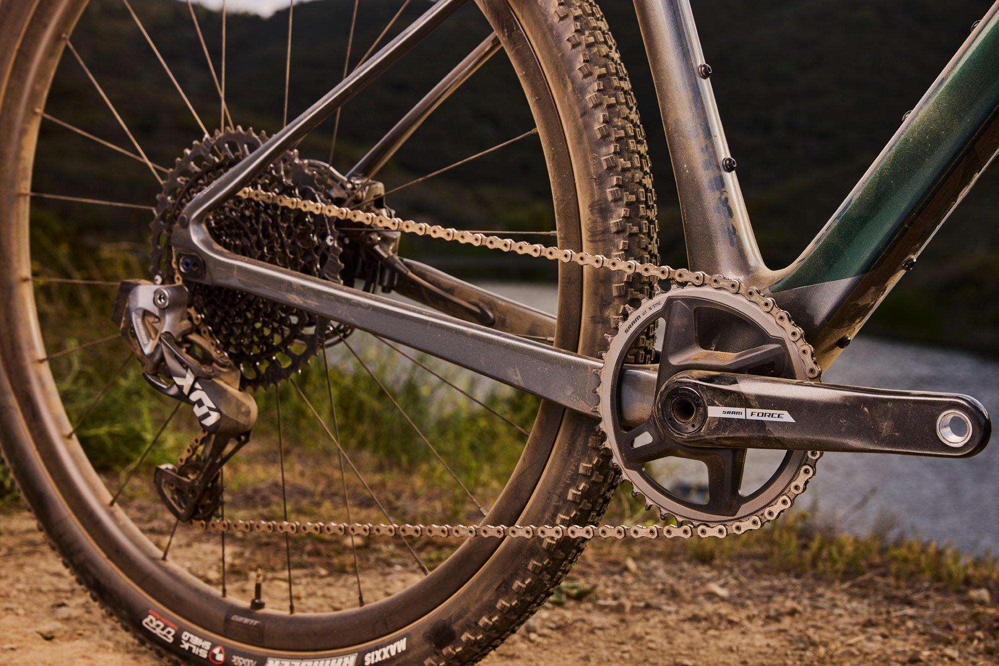 a close up of a bicycle chain and chainring on a dirt road