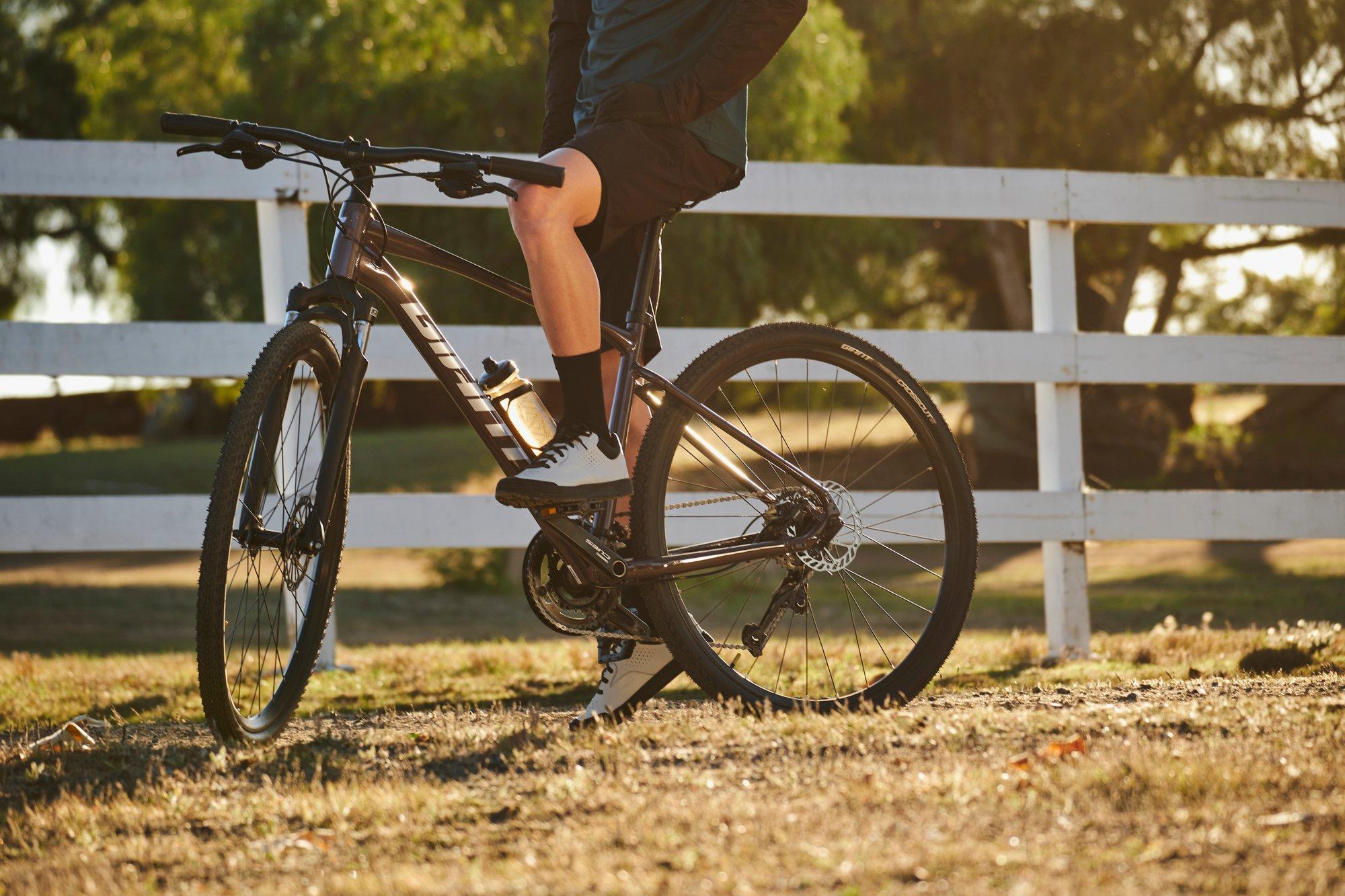 a man leaning on his bike while standing in front of a fence