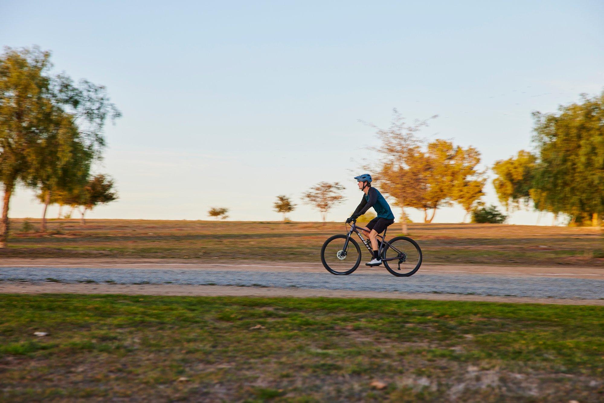 a man riding a bike on a road with trees and grass