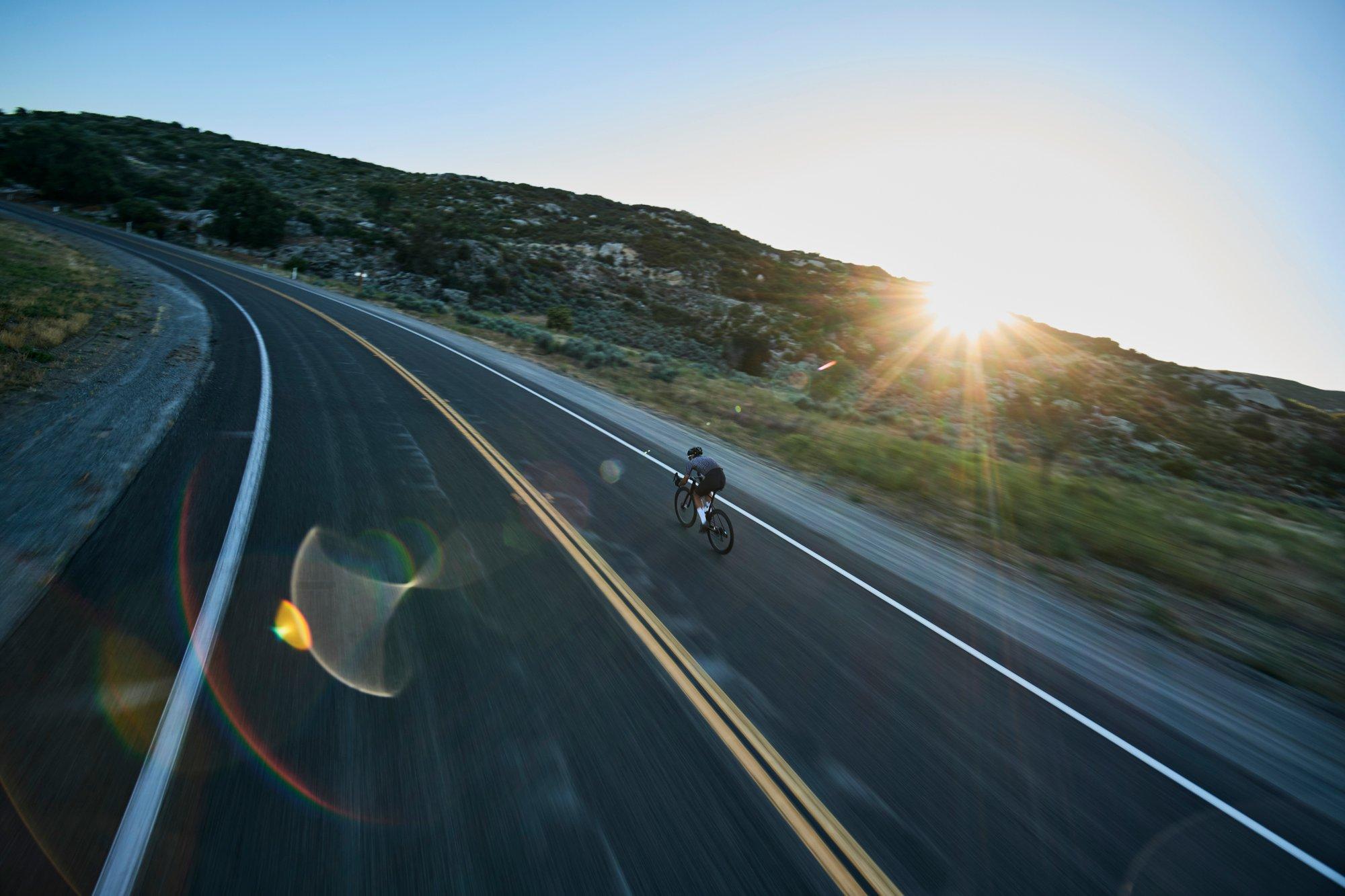 a person riding a bike down a road with the sun shining