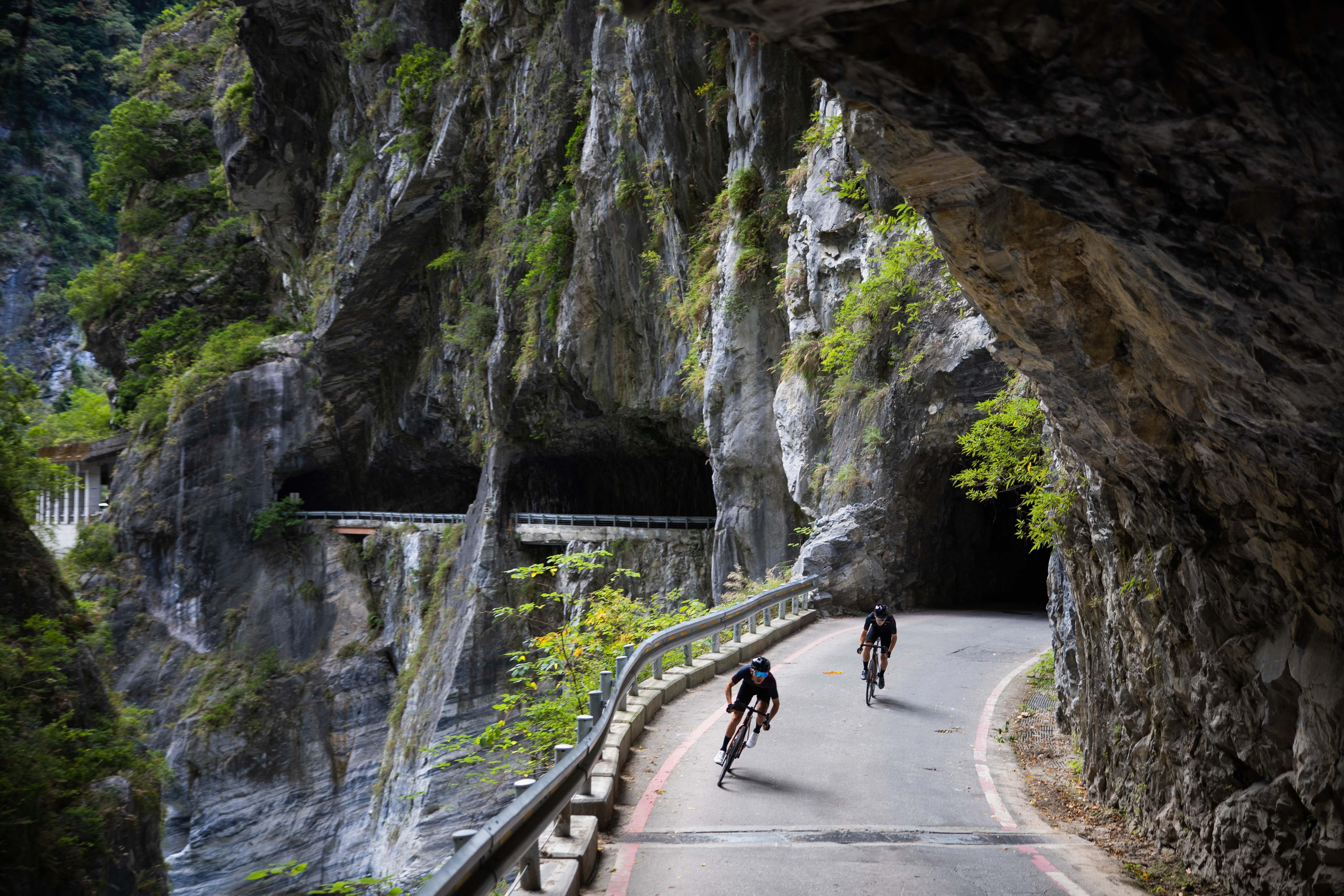 two people riding bikes down a narrow road in a tunnel