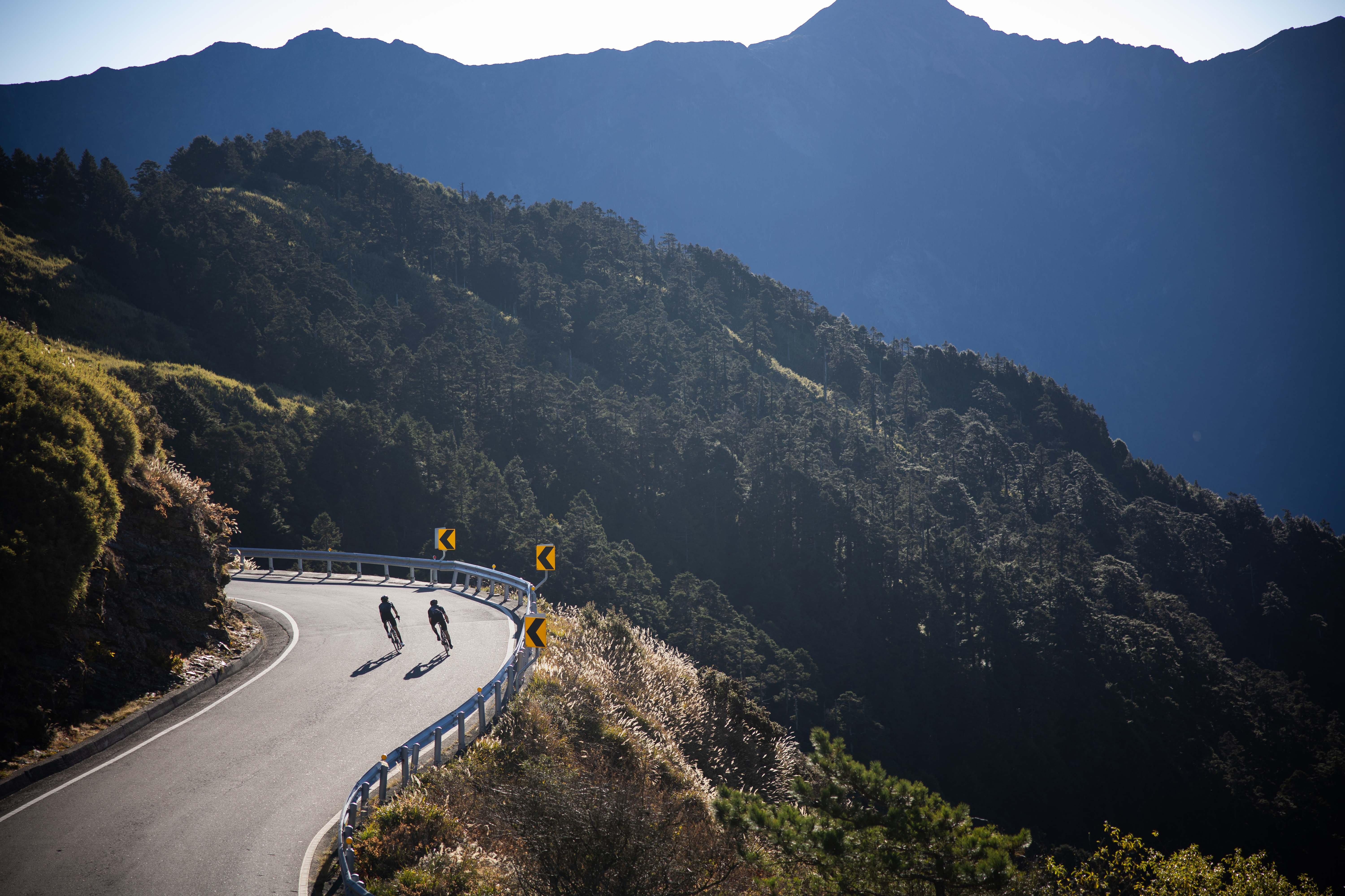 two people riding bikes on a winding road in the mountains
