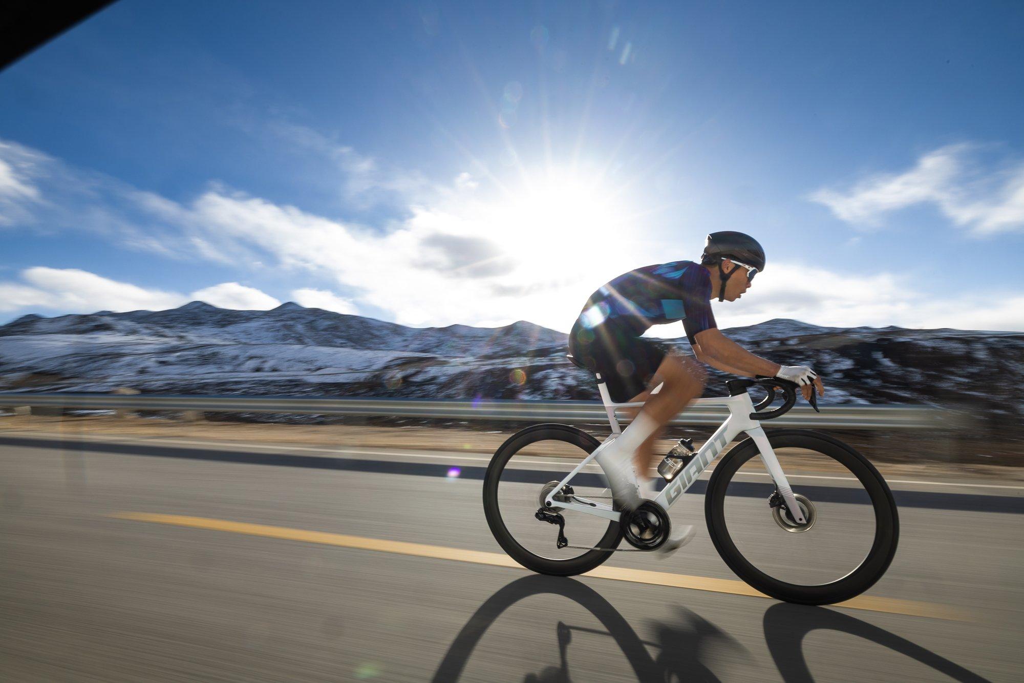 a man riding a bike on a road with mountains in the background