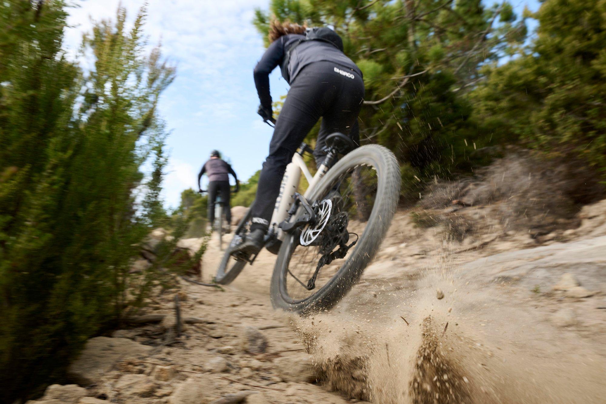 a couple of people riding bikes on a dirt trail