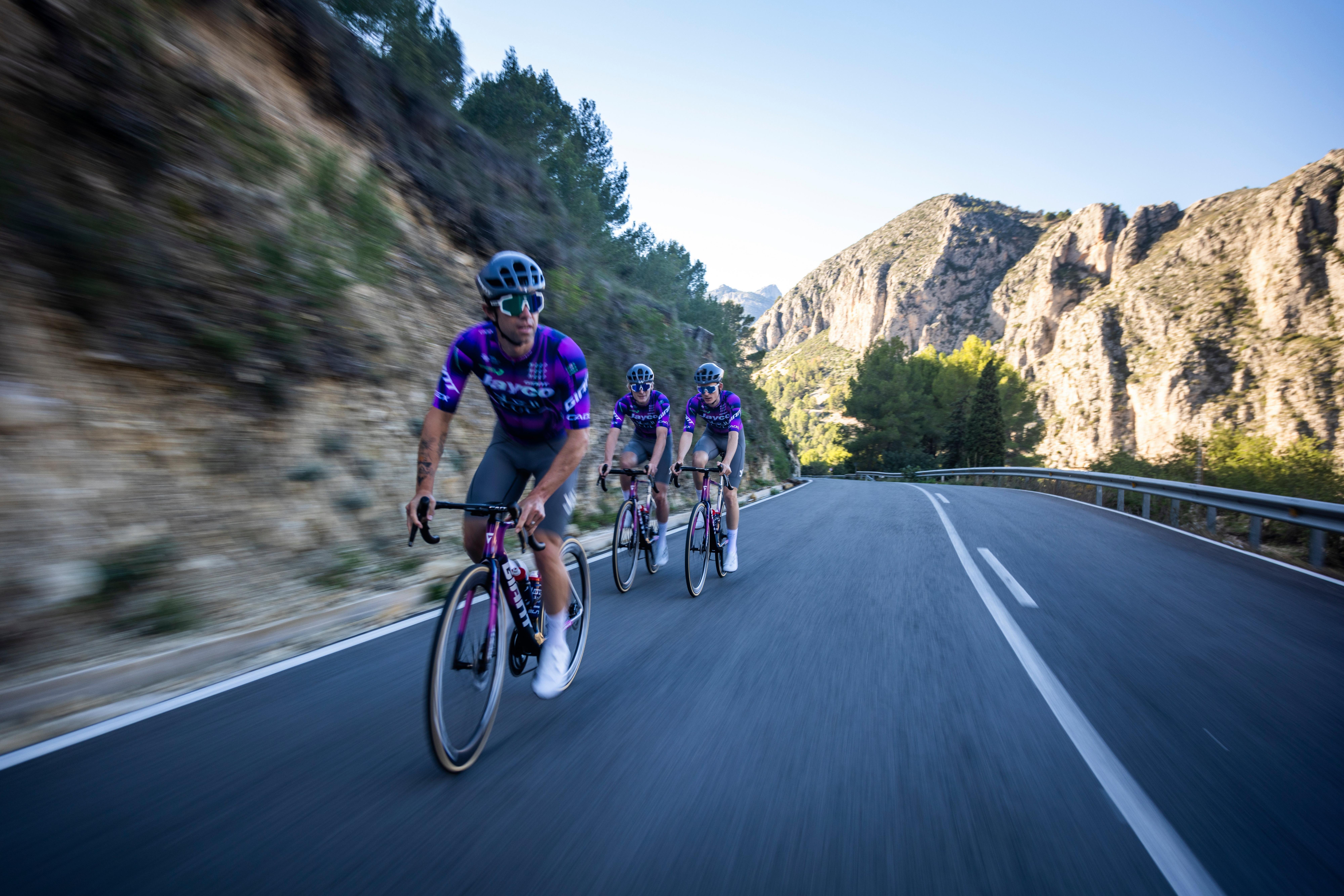 a group of cyclists riding down a road in the mountains