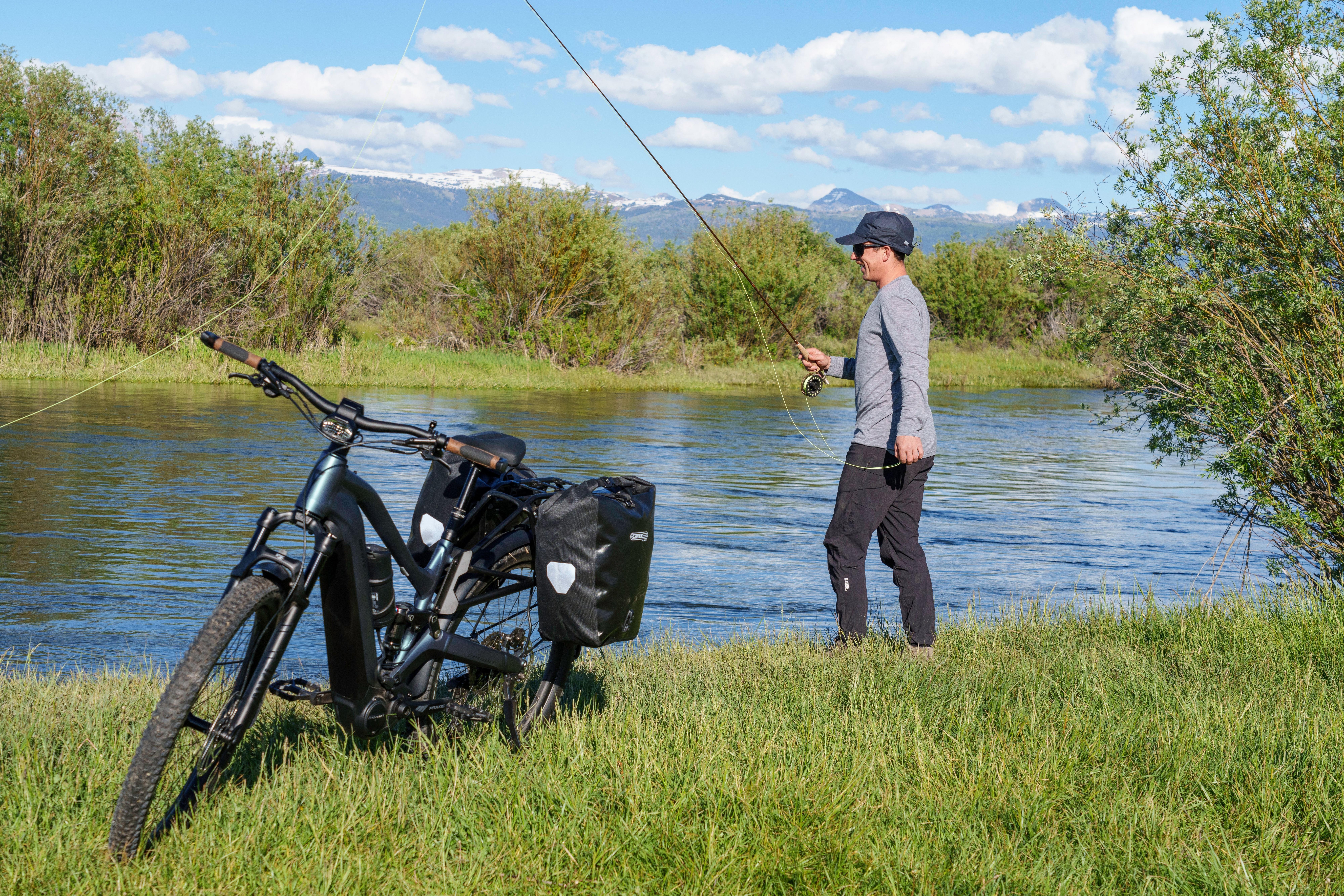 a man fishing by a river with a bicycle and a fishing pole