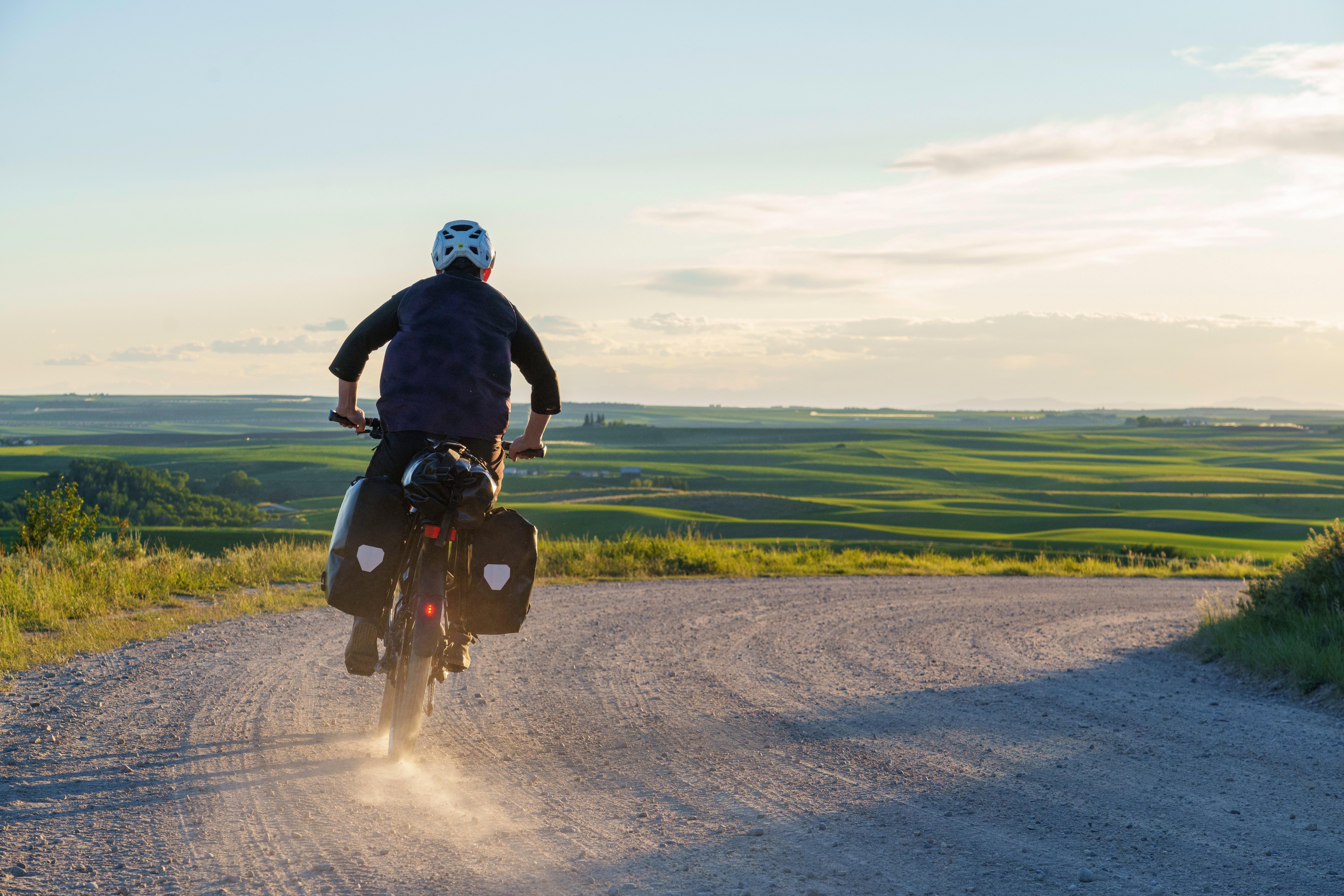 a man riding a bike down a dirt road with a dust cloud behind him