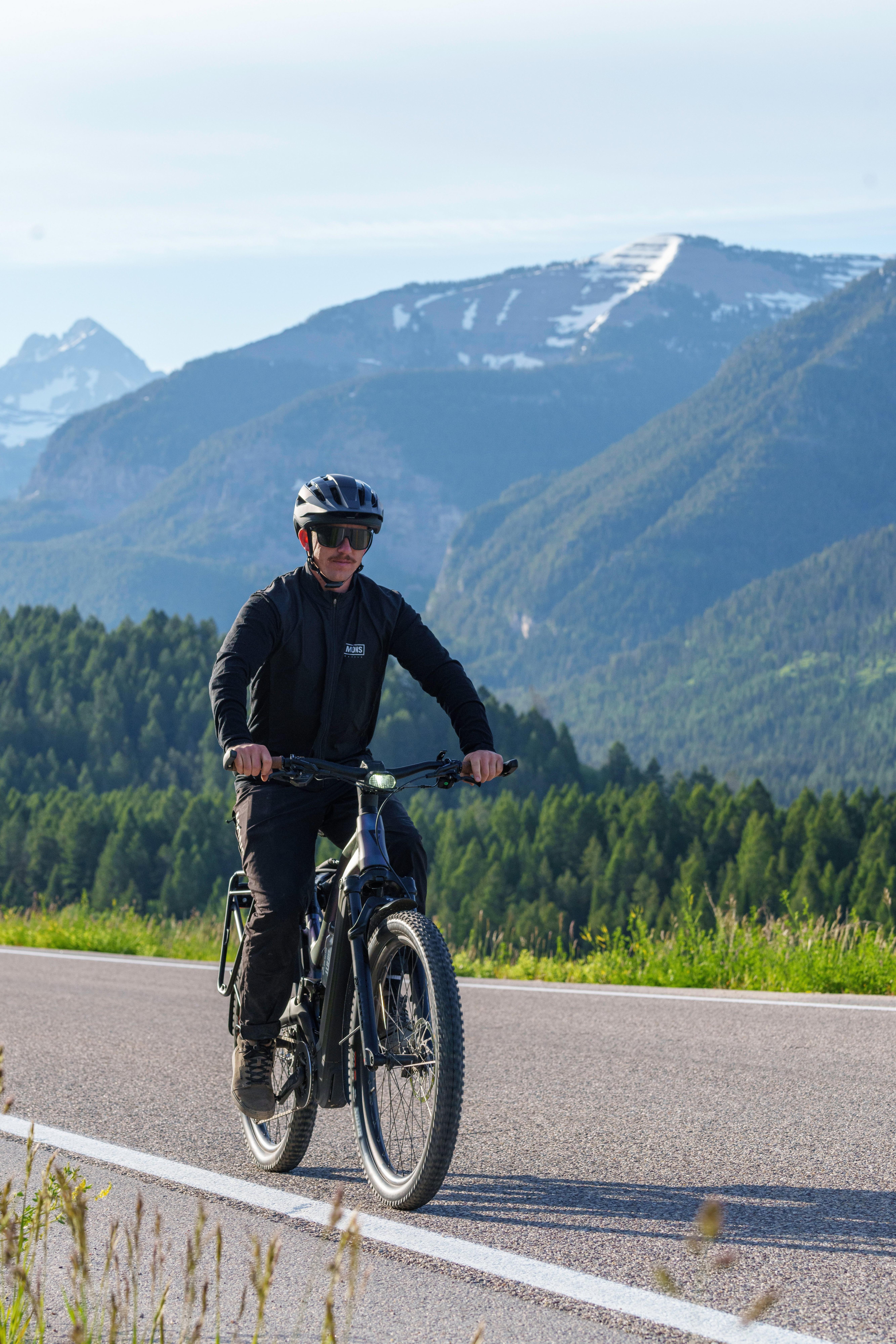 a man riding a bike on a road with mountains in the background