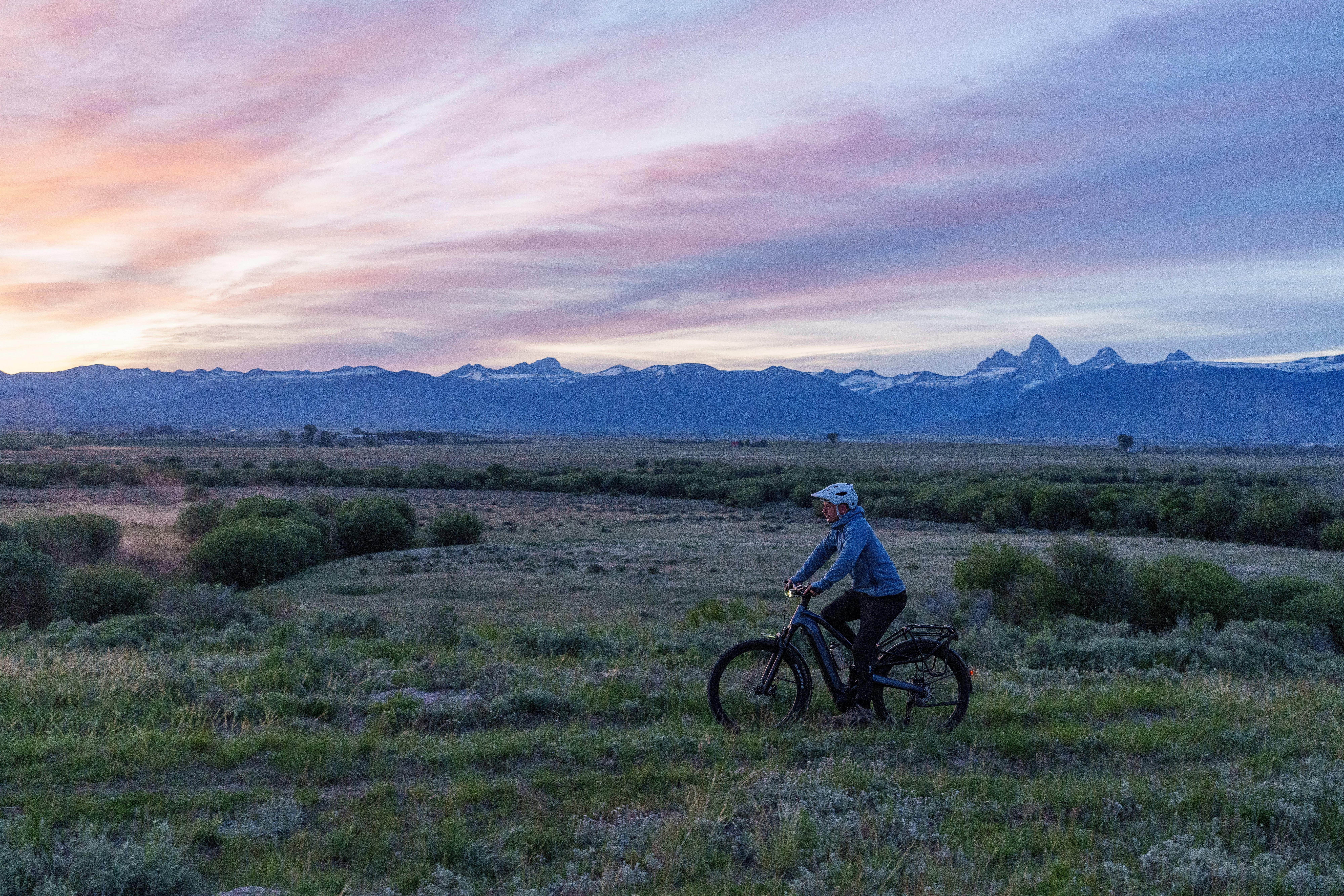 a person riding a bike in a field with a sunset in the background