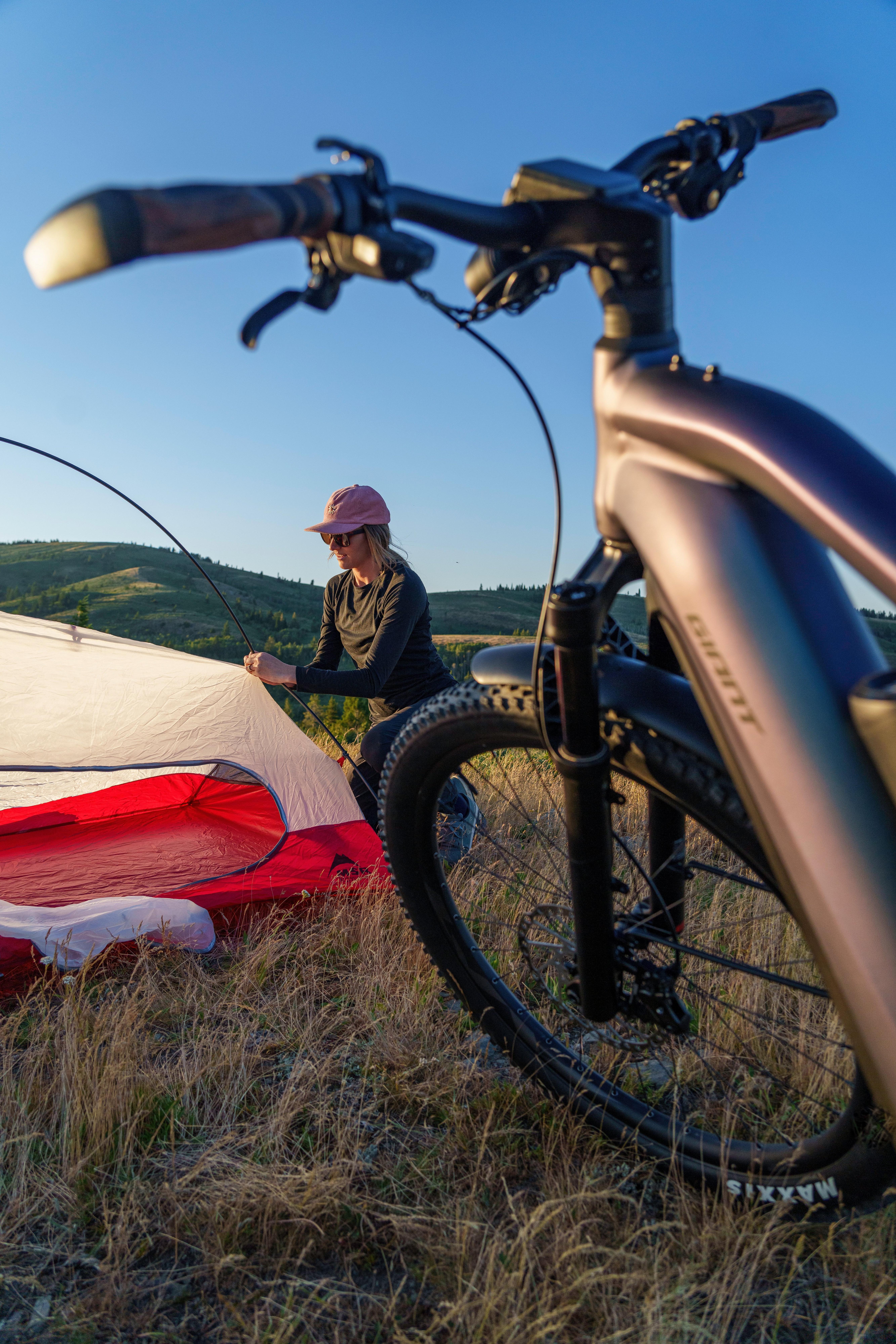a person setting up a tent in a field with a bicycle