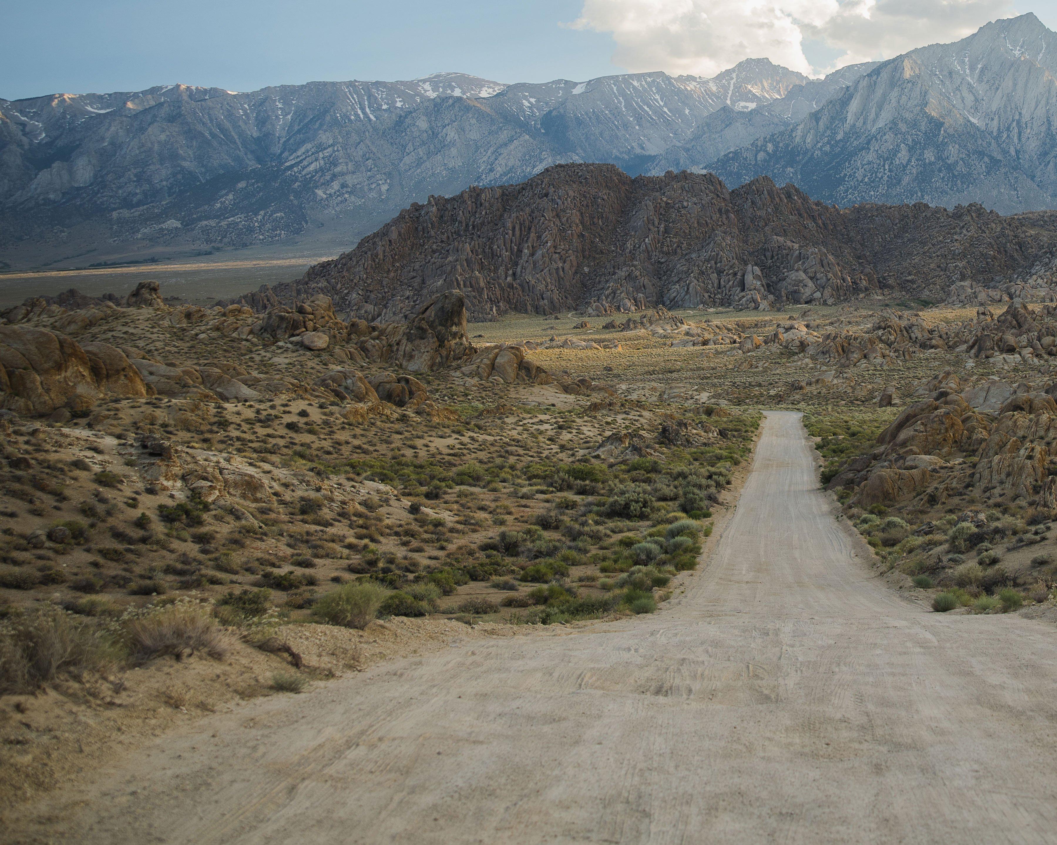 a dirt road leading to a mountain range in the distance