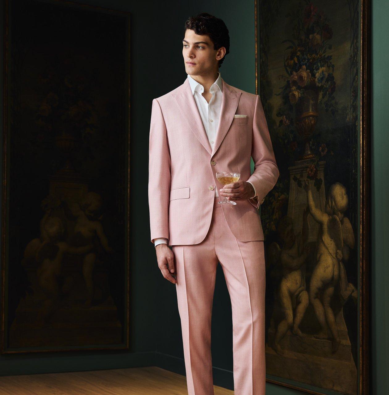 Un homme portant un complet beige clair avec une chemise blanche, une pochette de costume et une cravate bleu pâle