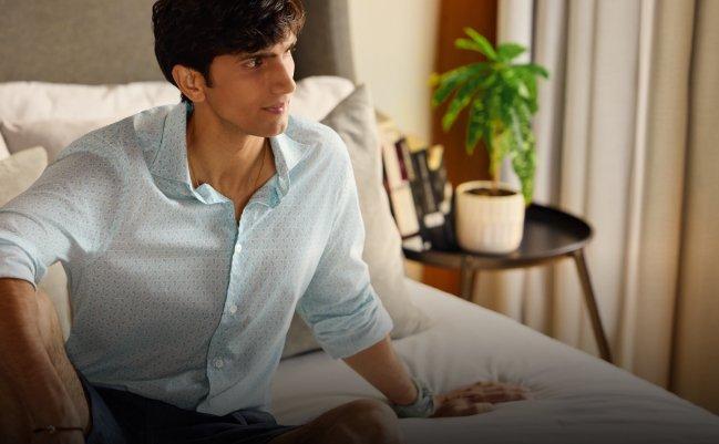Un homme portant une chemise à motifs bleu pâle avec des lunettes de soleil brunes