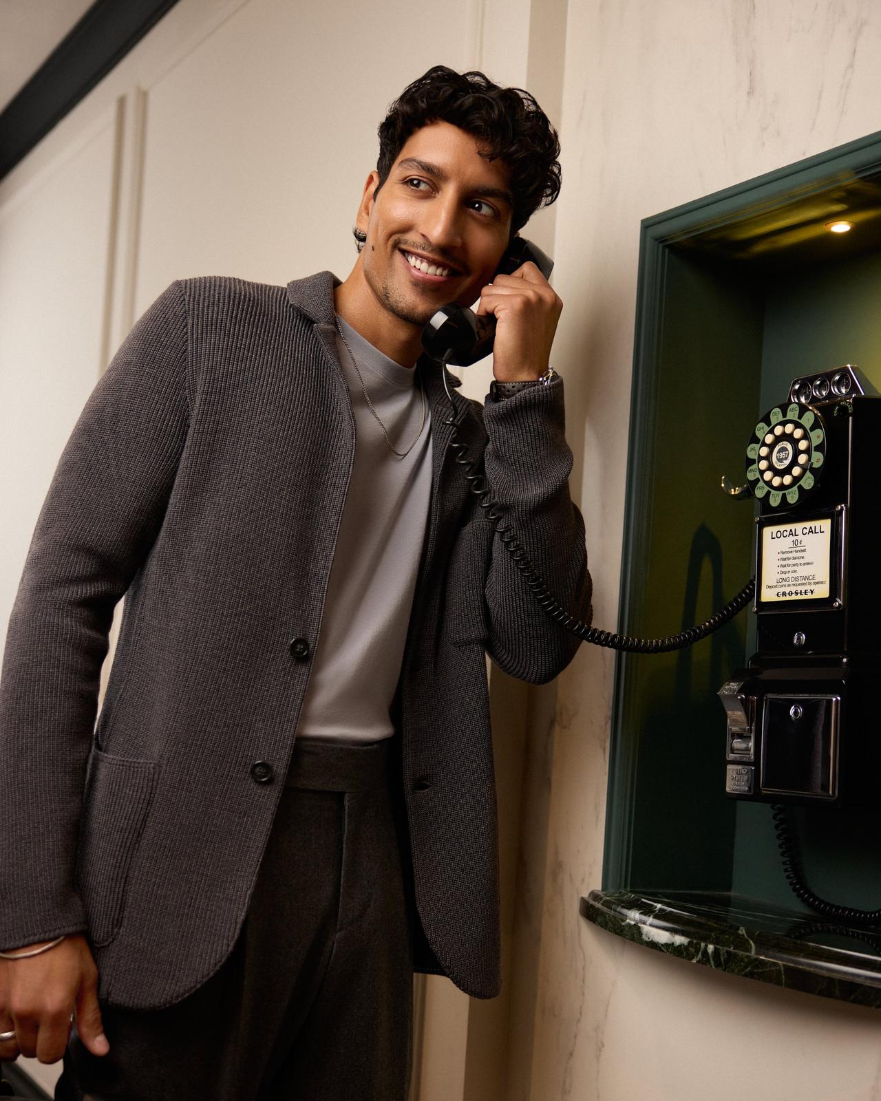 a male model wearing black pants, a grey sport jacket talking on the phone