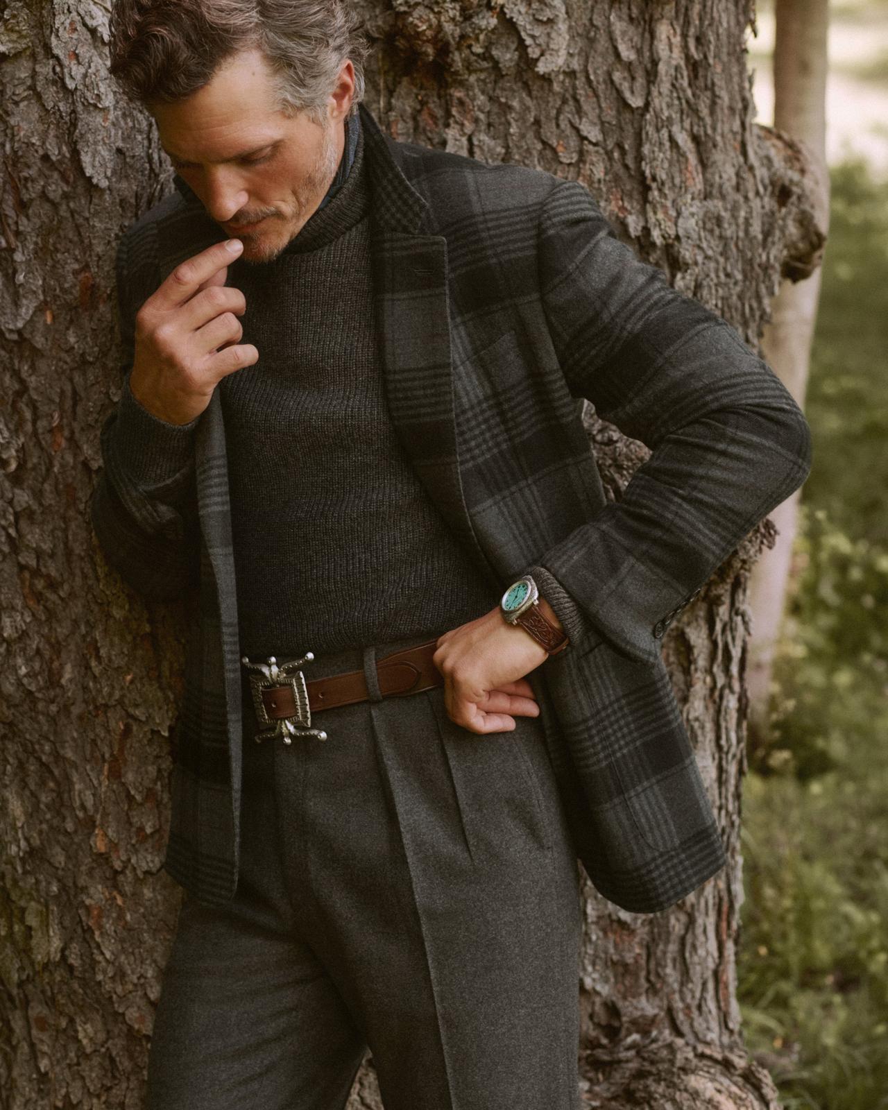 Man leaning against a tree wearing a grey plaid wool blazer, charcoal turtleneck, and pleated flannel trousers by Ralph Lauren Purple Label, FW26 collection