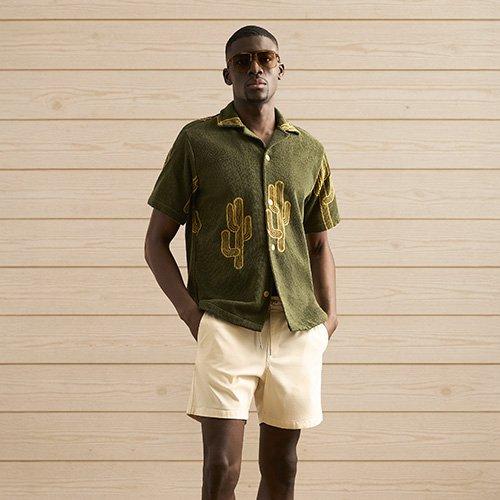 Un homme portant une chemise verte et un short blanc devant un chalet