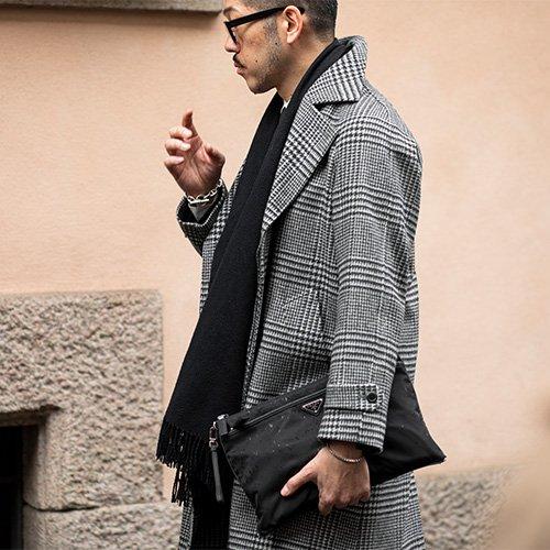 Un homme portant un manteau à carreaux, tenant un sac Prada, illustrant la Fashion Week homme de Milan