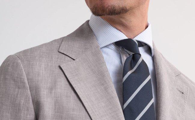 Close up of a model wearing a grey Brunello Cucinelli suit paired with a blue tie