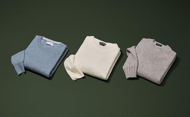 Three knit sweaters displayed on green backdrop