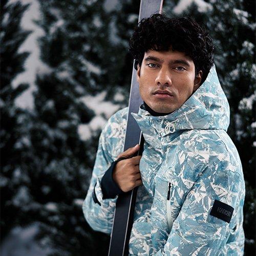 Male model wearing Mackage parka holding ski poles showcasing a ski escape