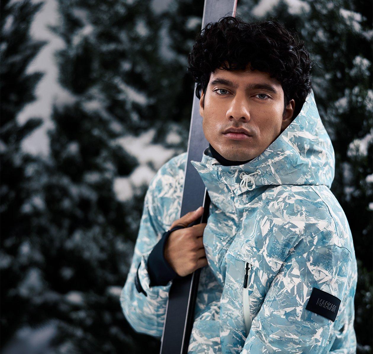 Male model wearing Mackage parka holding ski poles showcasing a ski escape