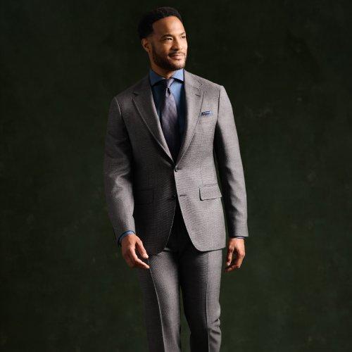 A man wearing a tailored grey suit paired with a navy dress shirt and tie