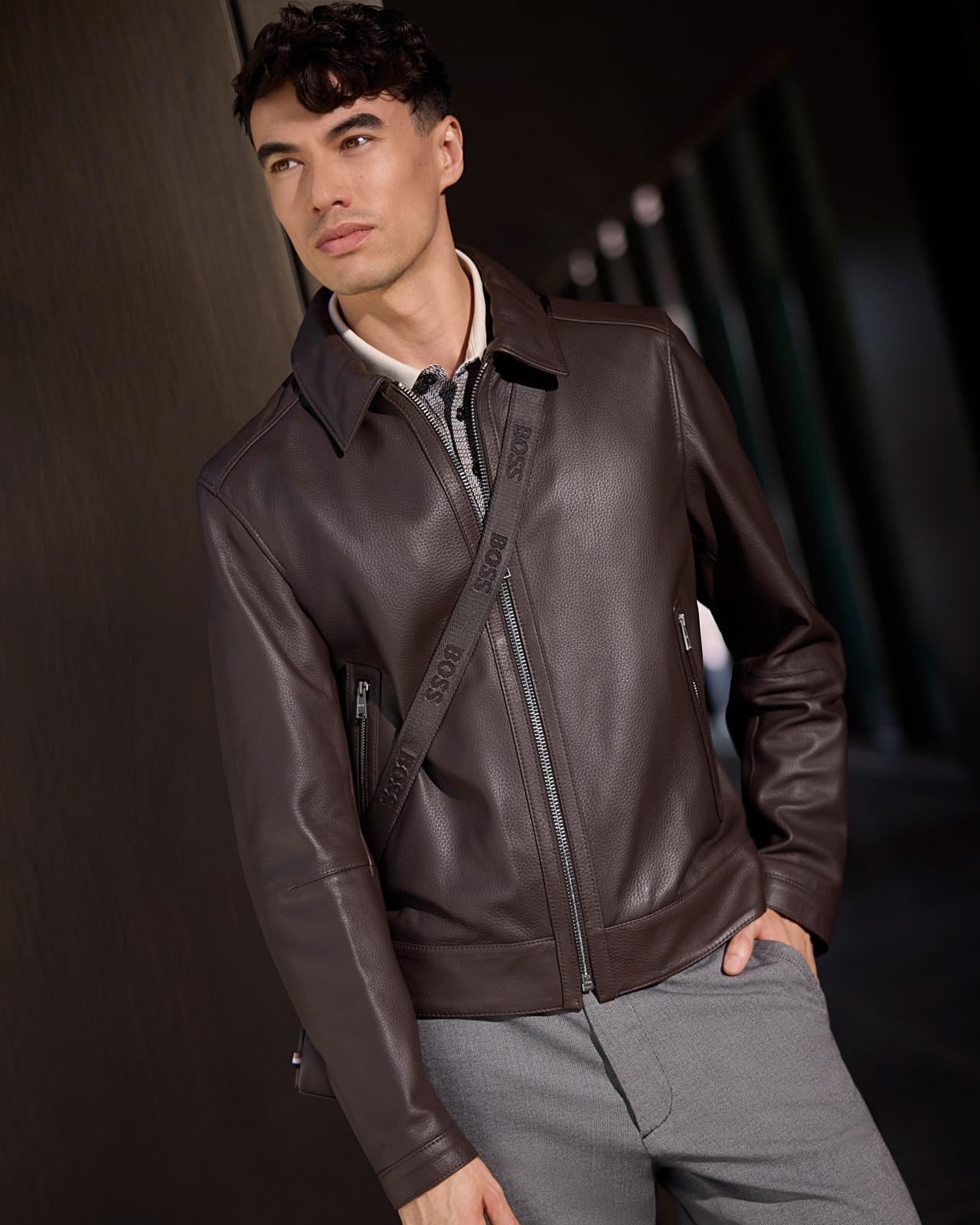 A male model wearing a brown leather jacket paired with medium grey slim-fit pants