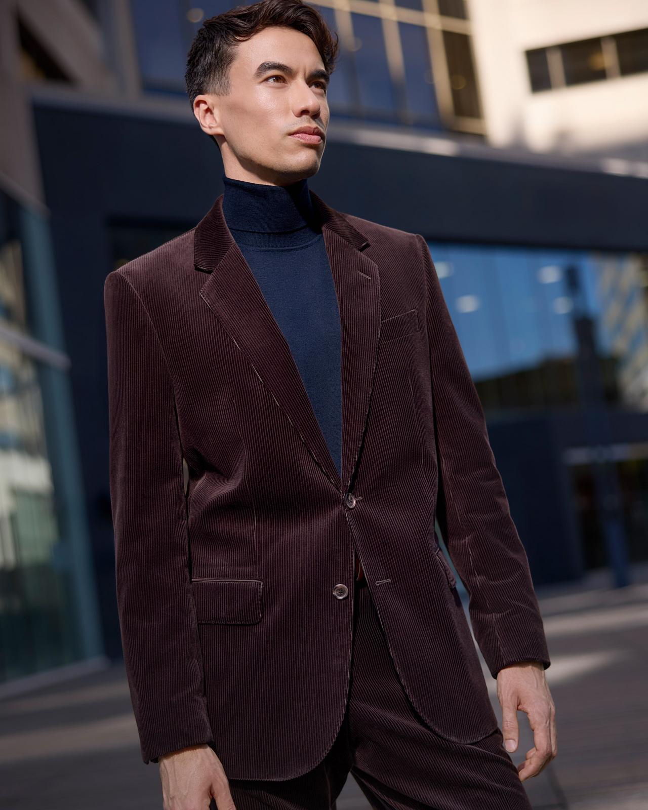 A male model wearing a BOSS dark burgundy velvet sport jacket, navy blue wool sweater, and pleated strip dress pants