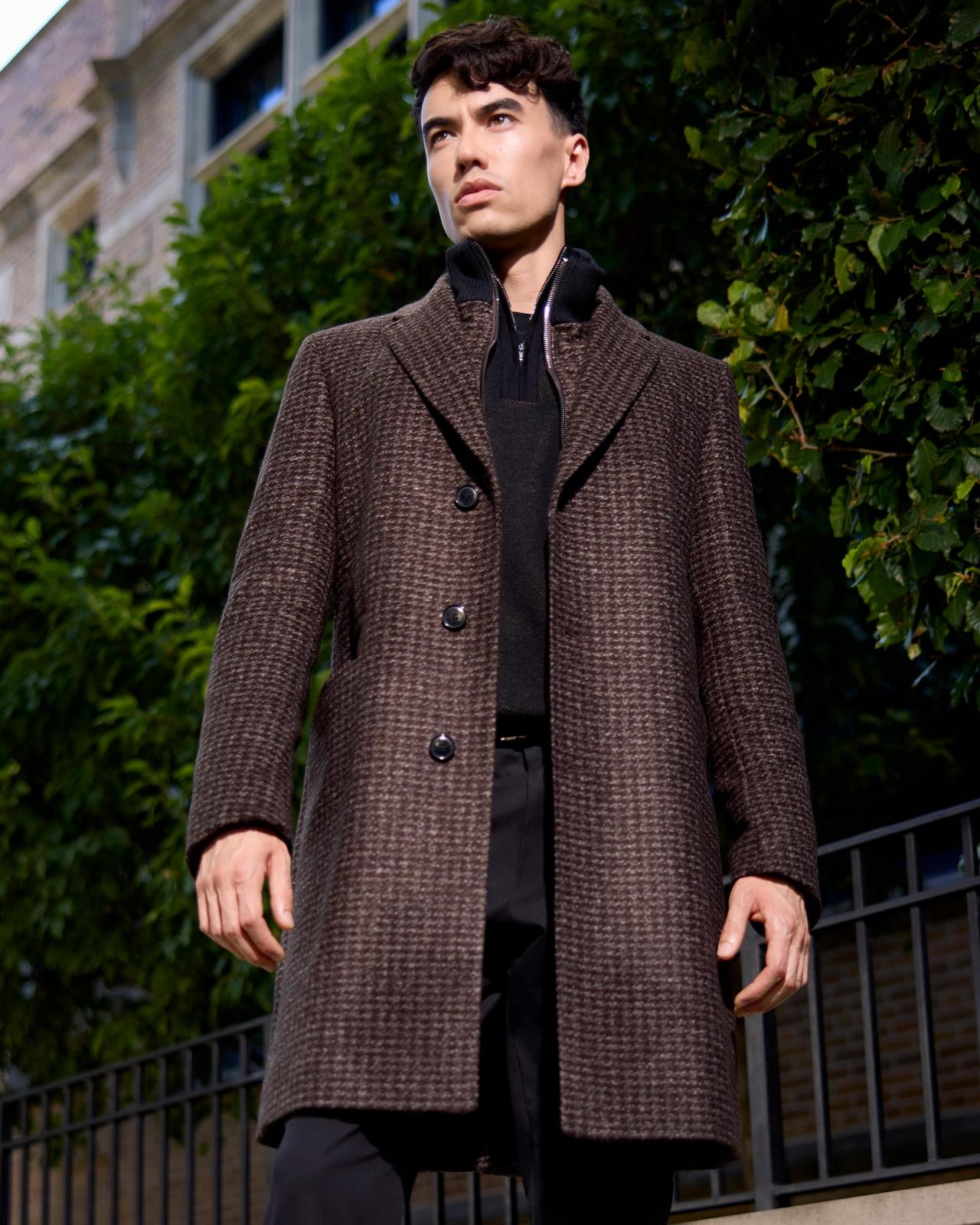 A male model wearing a dark brown BOSS coat, dark brown wool quarter-zip sweater, and black slim-fit pants