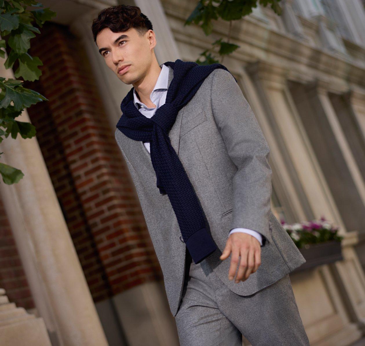 Homme portant un complet gris pâle BOSS avec un chandail bleu marine posé sur les épaules