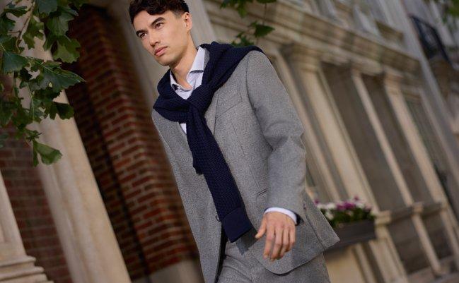 Man wearing a light grey BOSS suit with a navy sweater draped over his shoulders