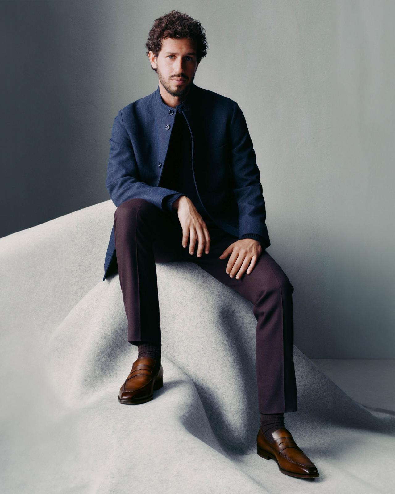 ChatGPT said:  Un mannequin masculin porte une veste bleu marine Berluti, assortie d’un pantalon bourgogne et de mocassins en cuir brun