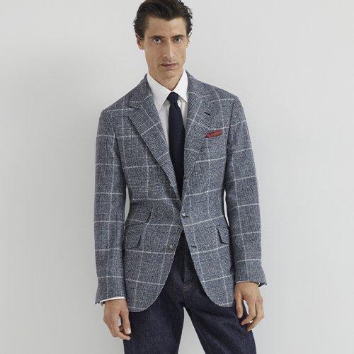 A man wearing a grey check sports jacket layered over a white shirt and tie