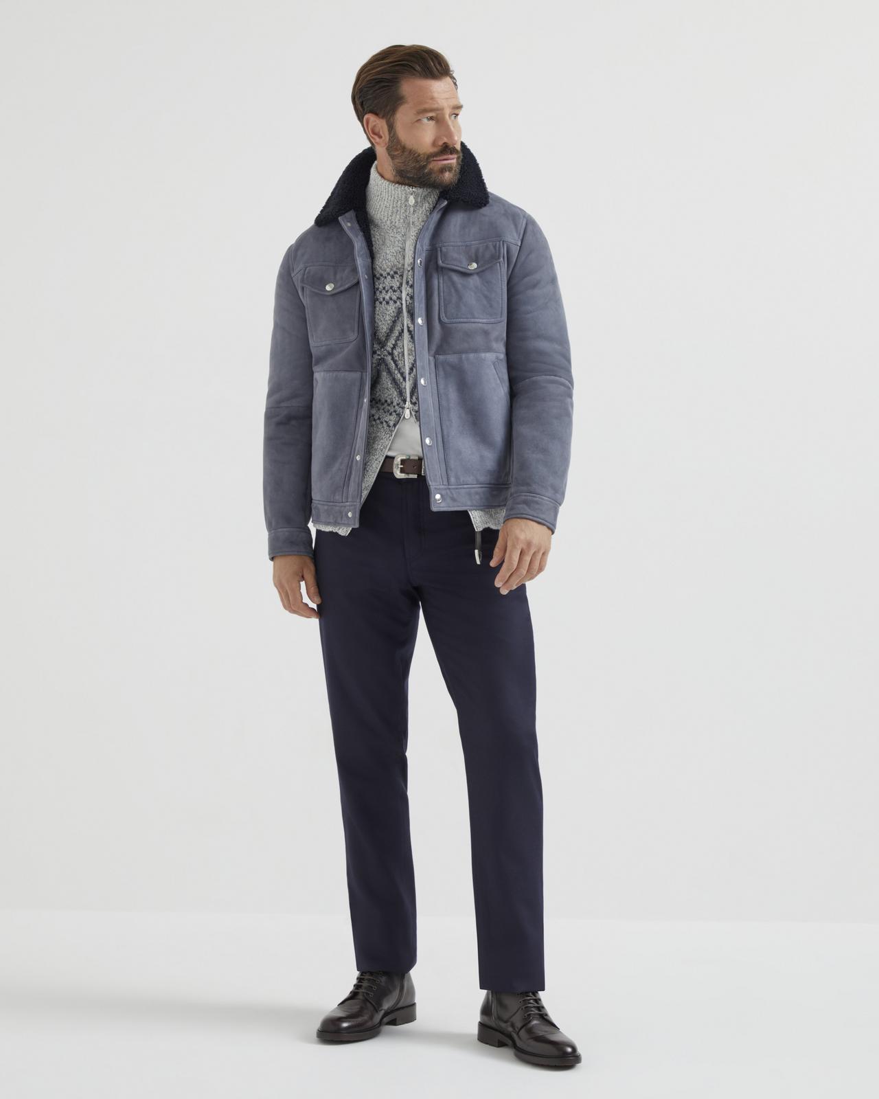 A man wearing a blue jacket layered over a grey sweater, paired with blue pants and black dress shoes