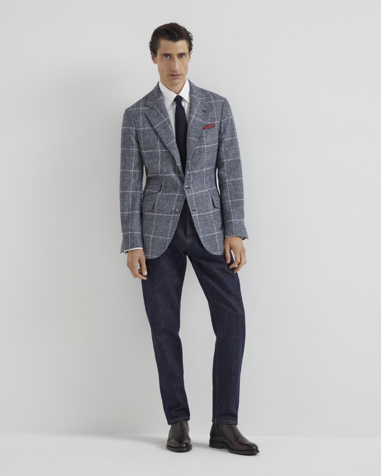 Un homme portant une veste sport grise superposée à une chemise blanche avec une cravate bleue, assortie à un pantalon bleu