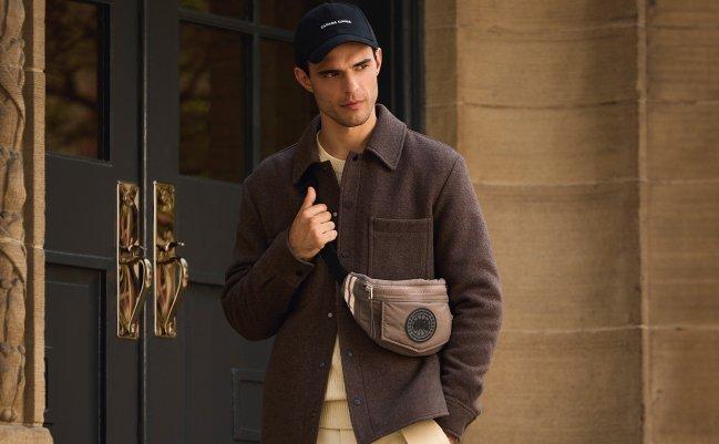 Un homme portant une surchemise mauve pâle avec un sac bandoulière