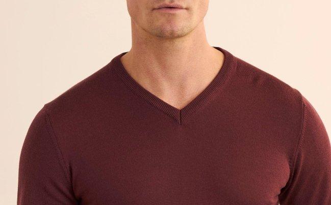 A model wearing a burgundy merino wool V-neck sweater