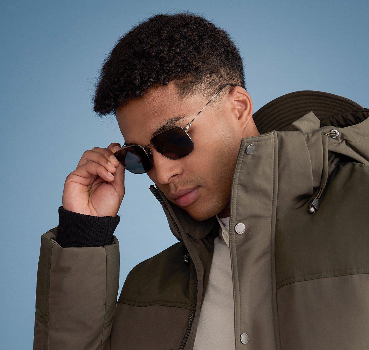 A man styled in a black jacket paired with sleek black sunglasses