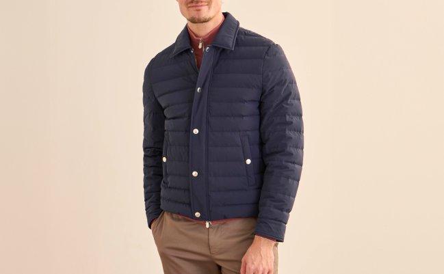 Un mannequin masculin porte un manteau matelassé léger bleu marine Brunello Cucinelli, assorti d’un pantalon brun