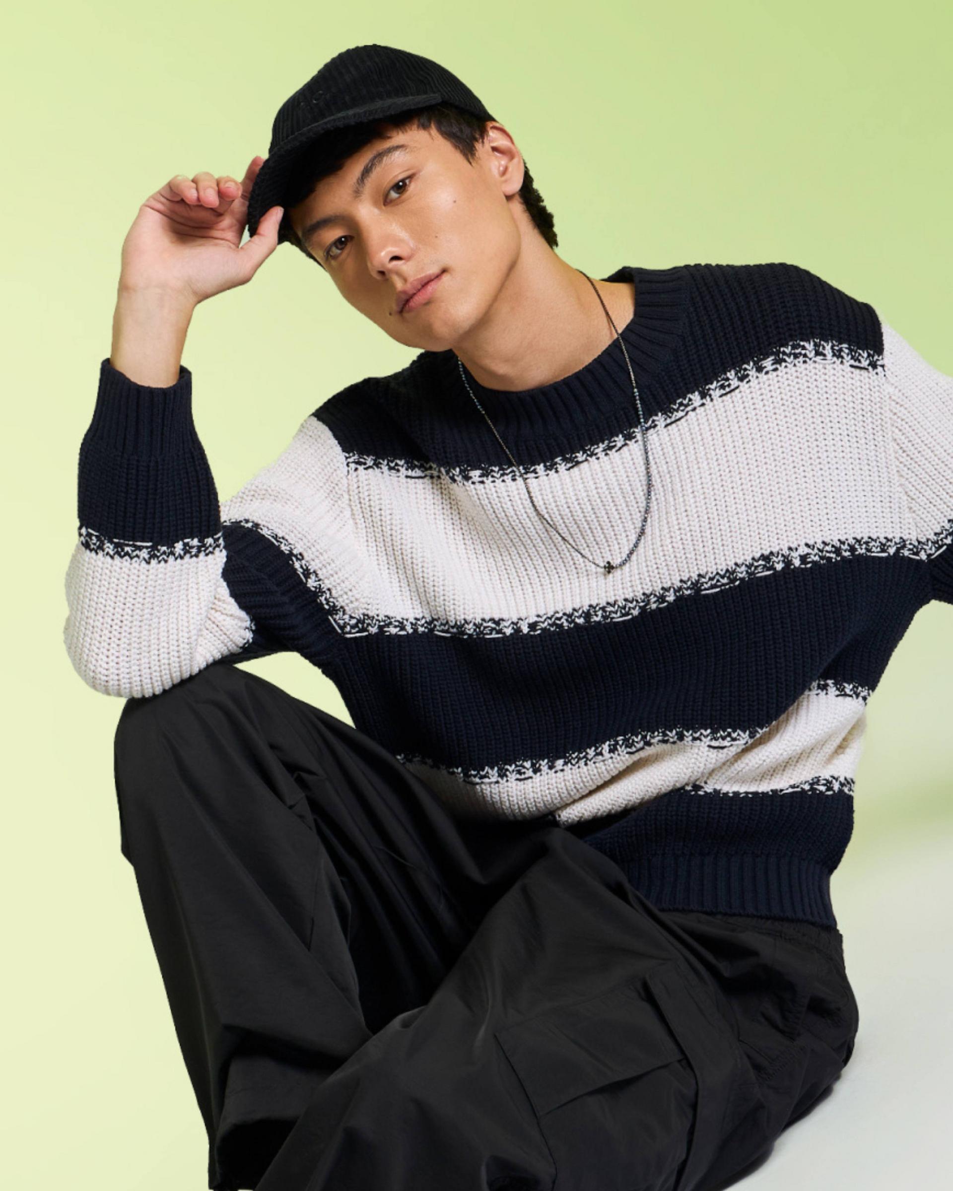 A male model wearing a black and white striped knit sweater styled with a hat