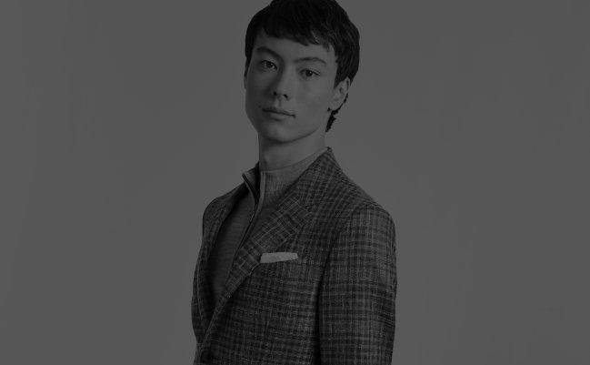 A man wearing a beige plaid sports jacket layered over a light dress shirt