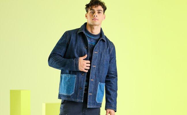 Man wearing a denim jacket with contrasting blue pockets, standing against a green background