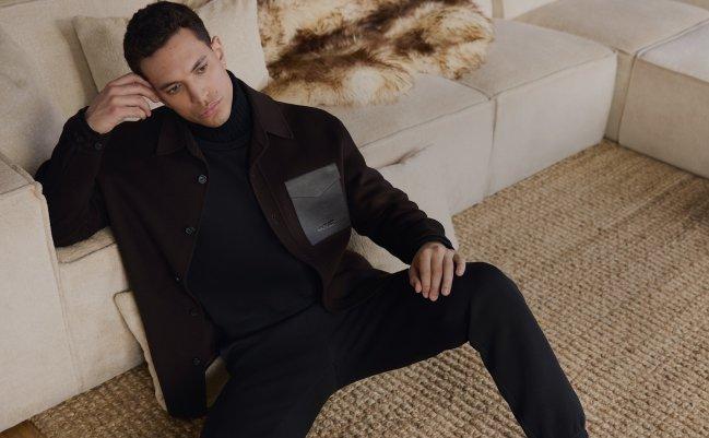 A man sitting near the couch wearing black jacket and pants