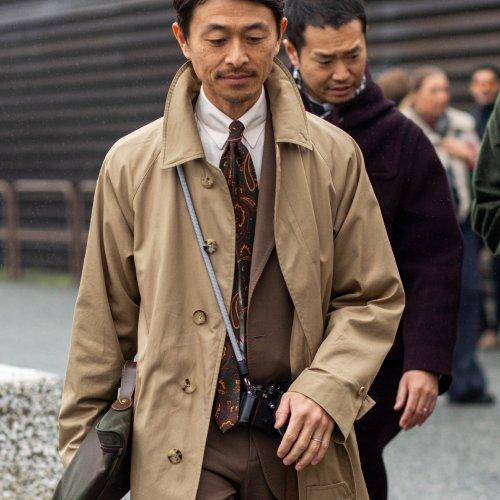 Un homme portant une veste beige chaud, une chemise blanche et une cravate brune