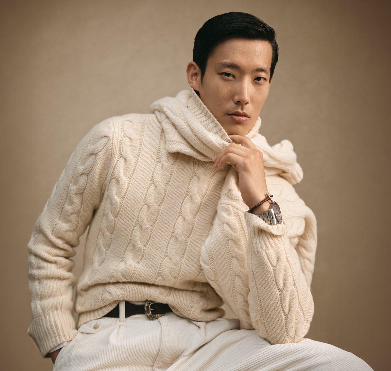 A man wearing a cream color sweater and pant with scarf